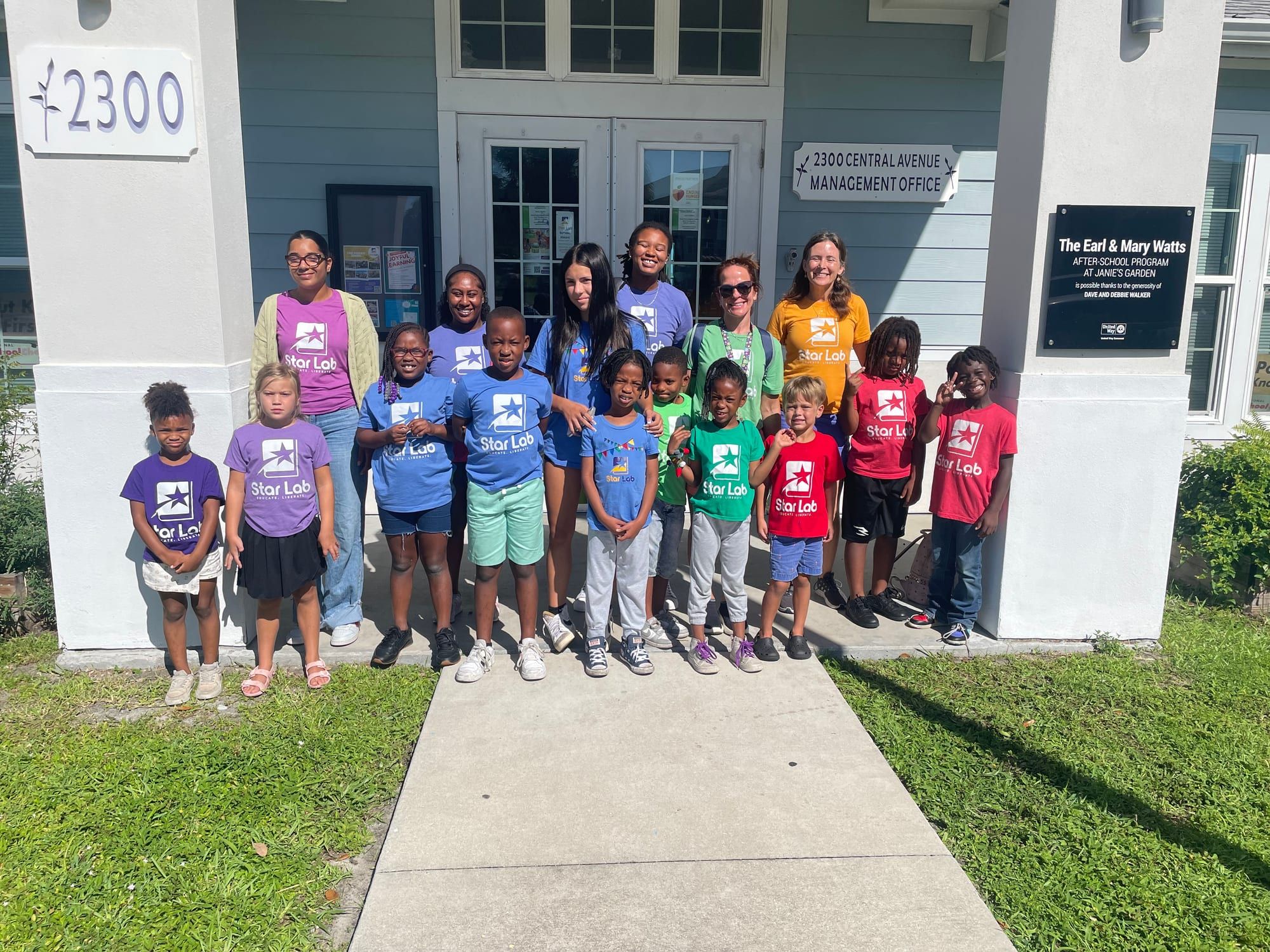 Children in purple, blue, green and red Star Lab T-shirts lined up with their teachers outside the light-blue building marked 2300.