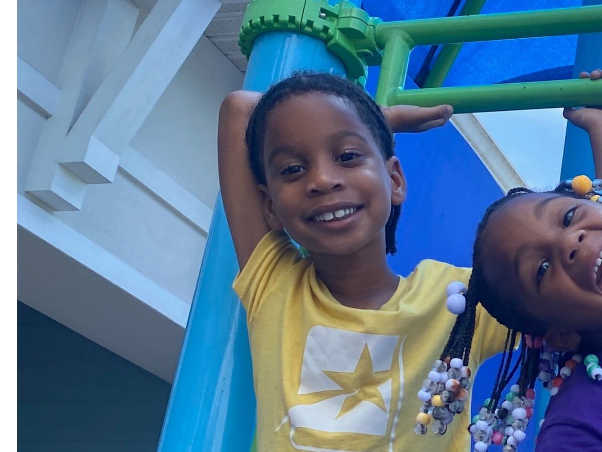 Two laughing girls on a blue playground slide, one in a yellow Star Lab T-shirt.